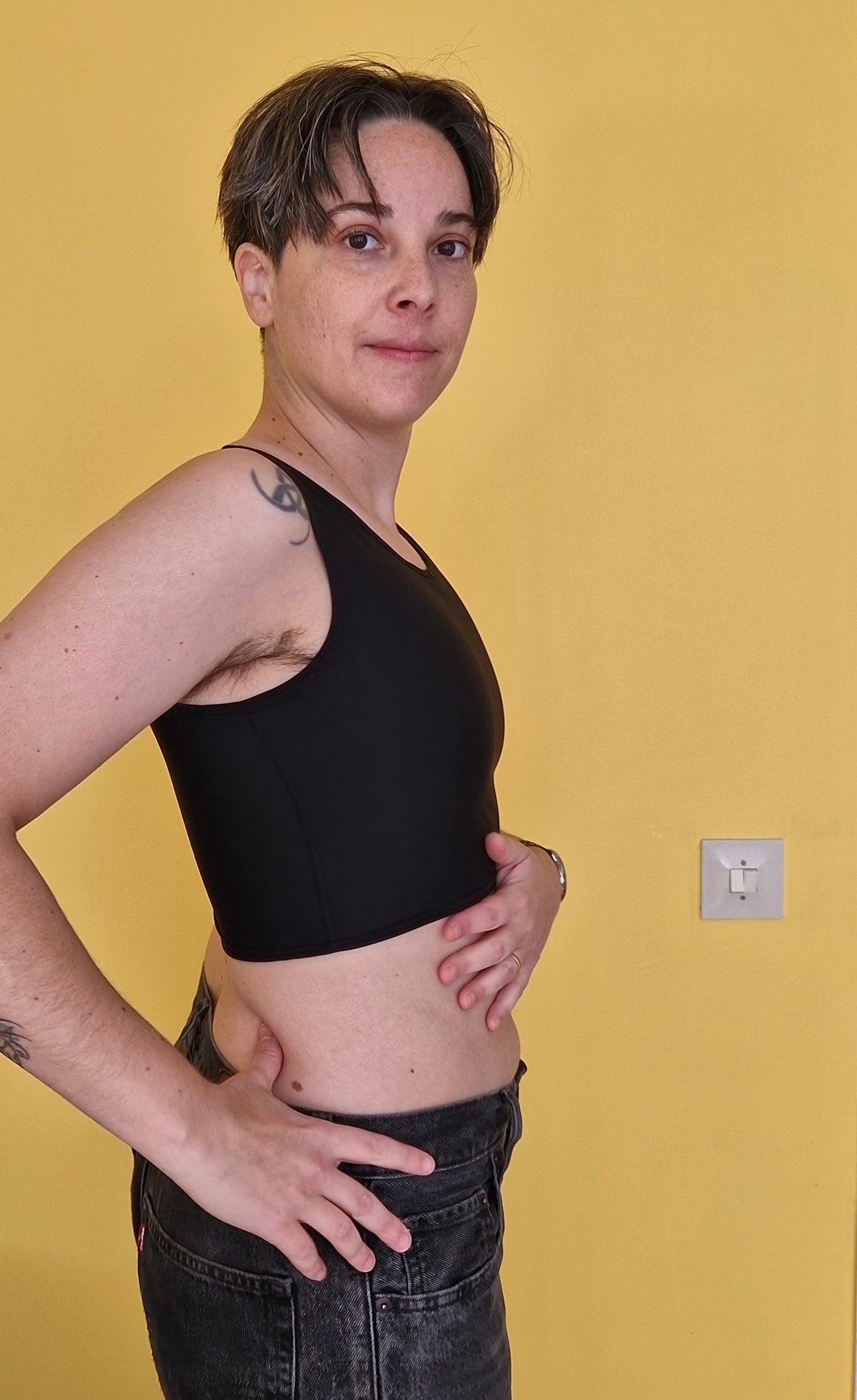 A trans nonbinary person wearing UNTAG black short chest compression binder. side view.