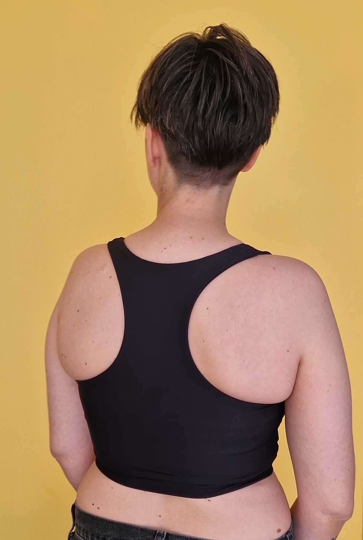 A trans masc person wearing a safe and comfortable racerback chest binder. View from back
