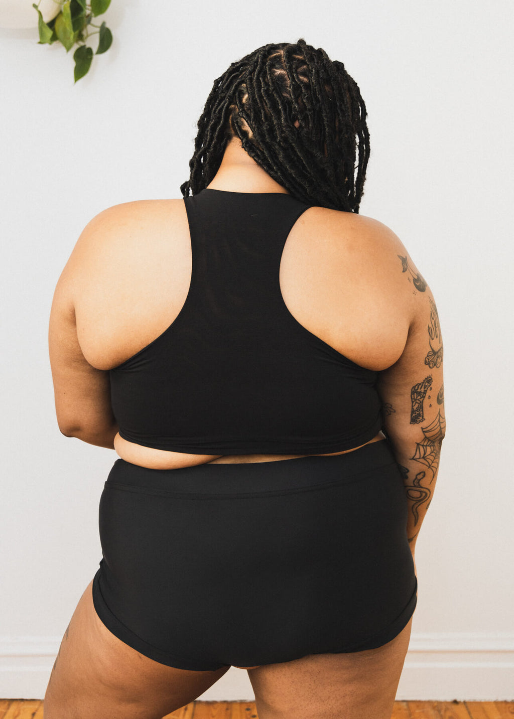 A person wearing a black soft binder from Origami Customs. Back view. Plus size.