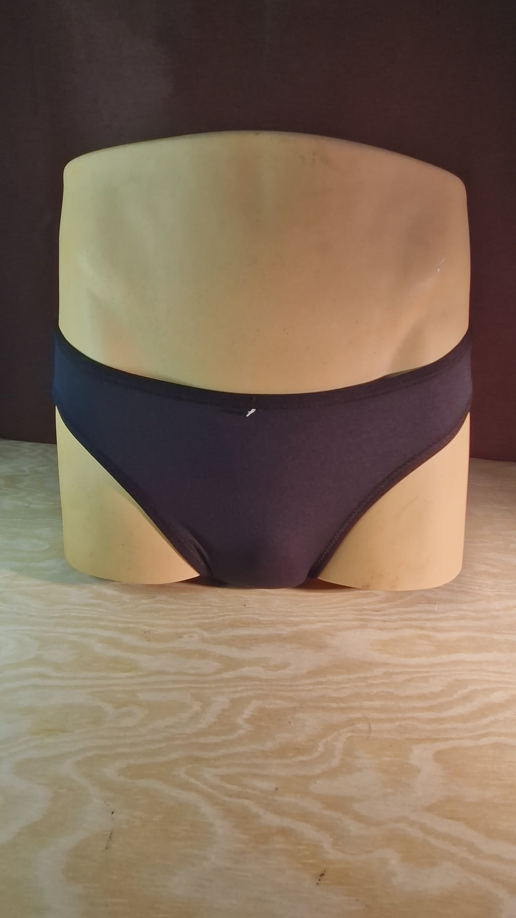 A half-bust mannequin wearing tucking thong in black. It spins to show front and back.