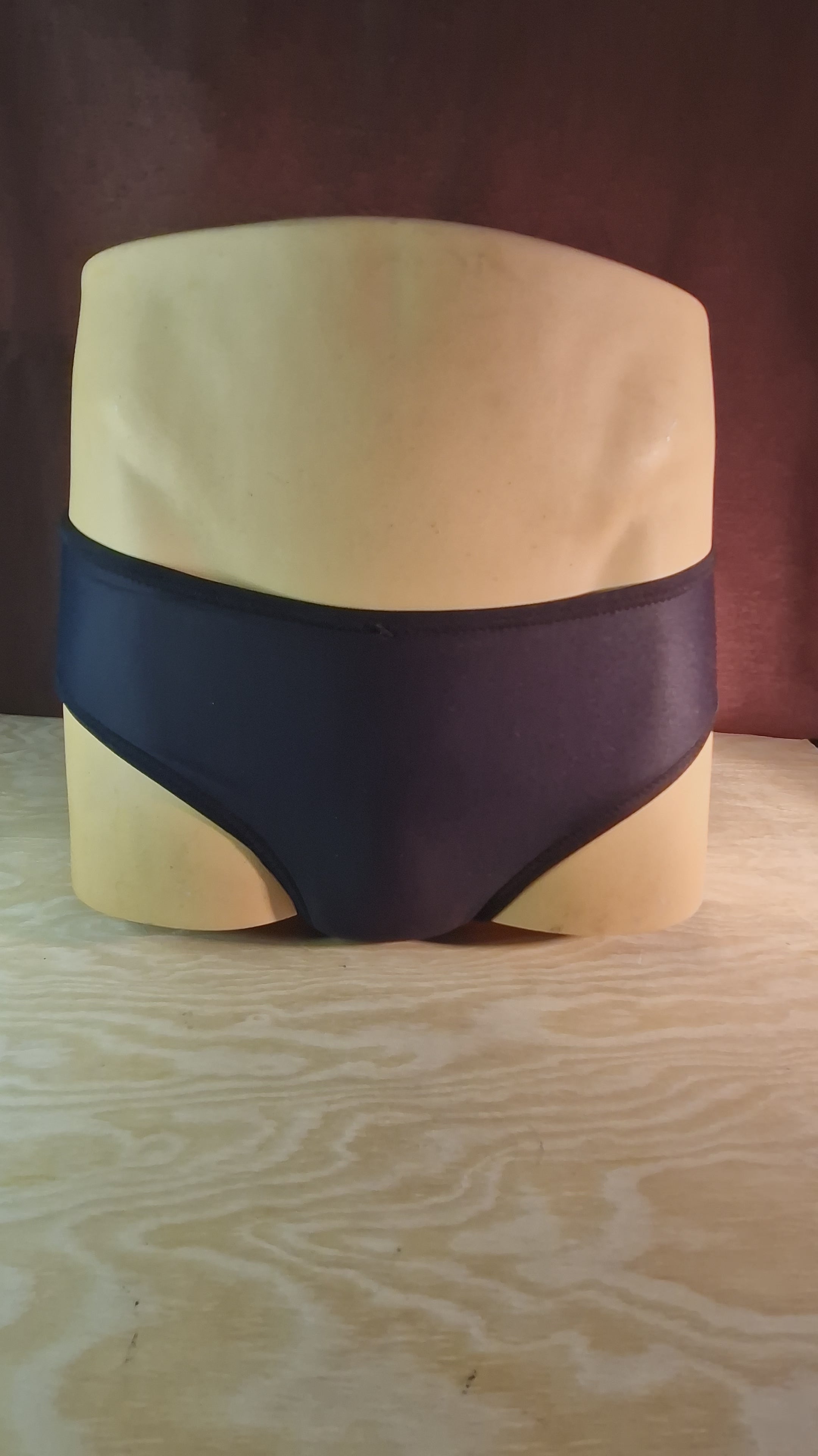 A half-bust mannequin wearing tucking panties in black. It spins to show front and back.
