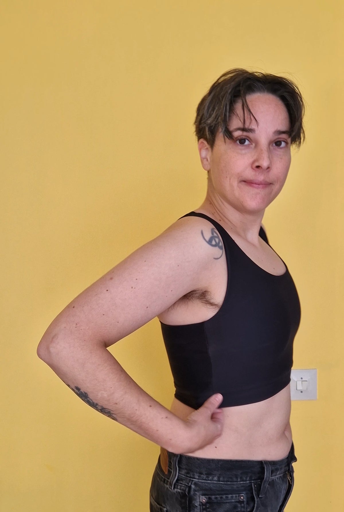 A nonbinary person wearing a comfortable black chest binder. View from the side.