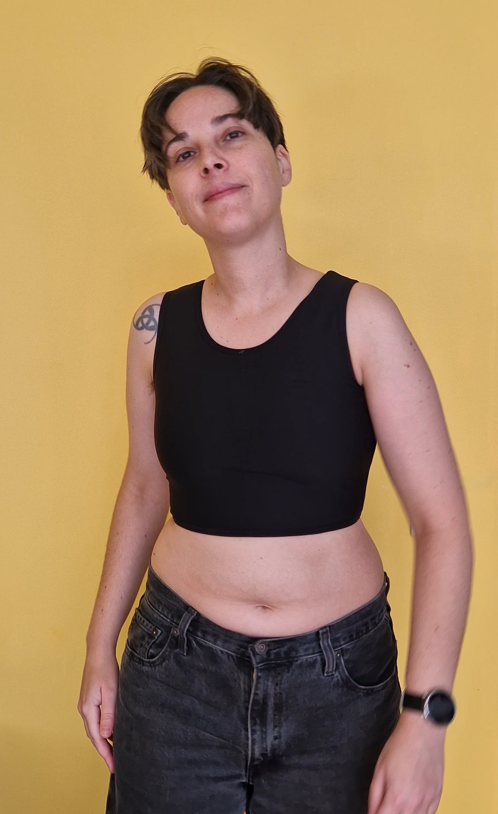 A trans nonbinary person wearing a black short chest compression binder. Front view.