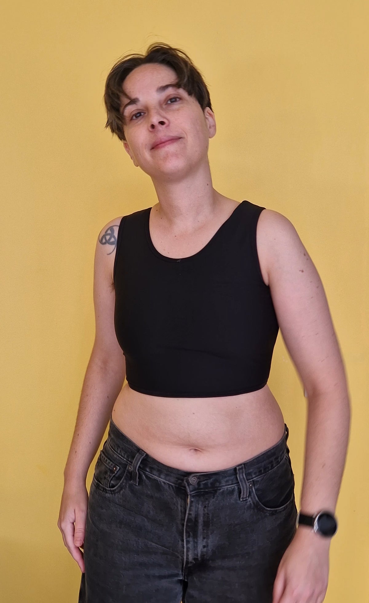 A trans nonbinary person wearing a black short chest compression binder. Front view.