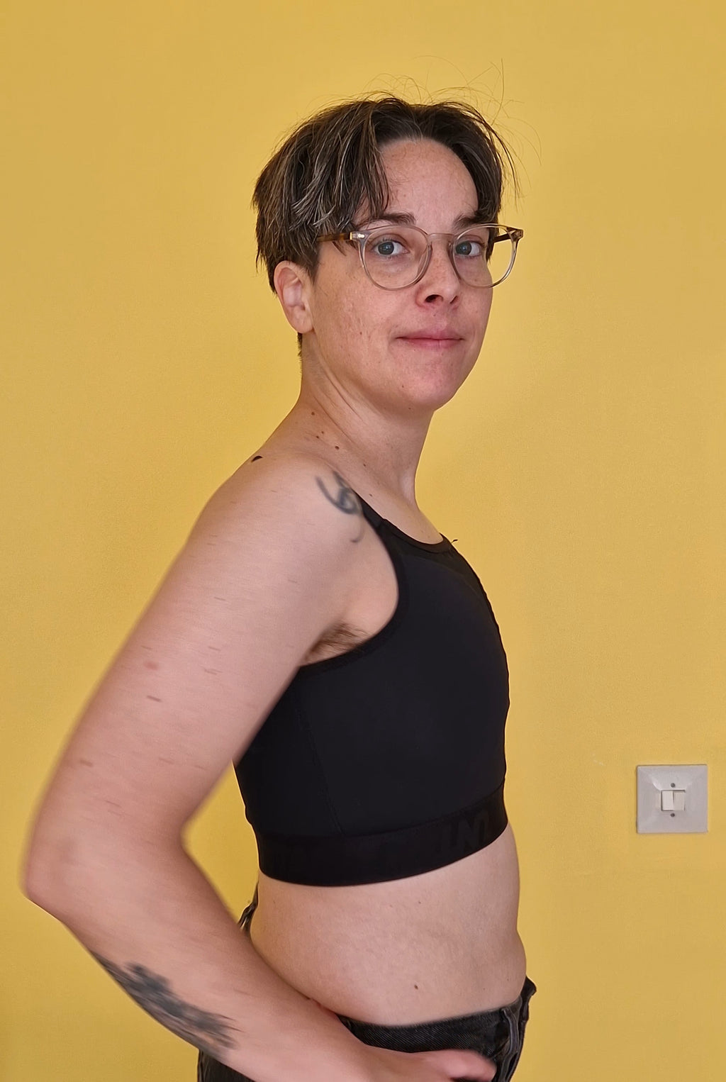 A nonbinary person wearing a black gym safe chest binder made for trans masc, trans man, ftm, drag kings. Side view.