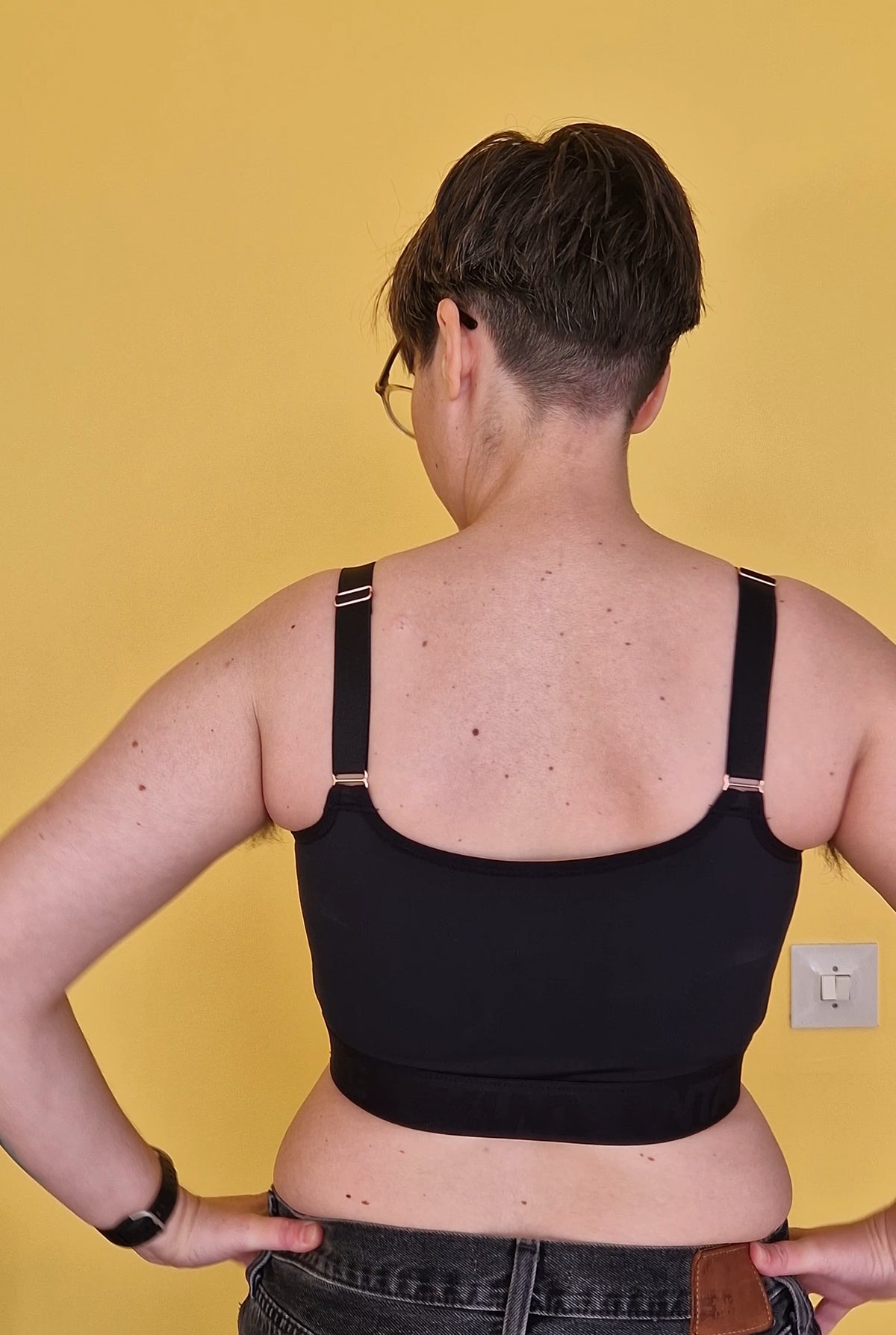 A nonbinary person wearing a black gym safe chest binder made for trans masc, trans man, ftm, drag kings. Back view.